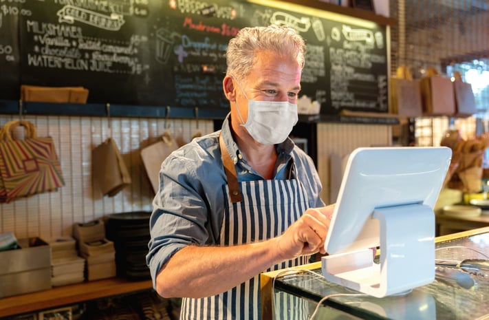 Middle-aged business owner uses tablet while wearing mask