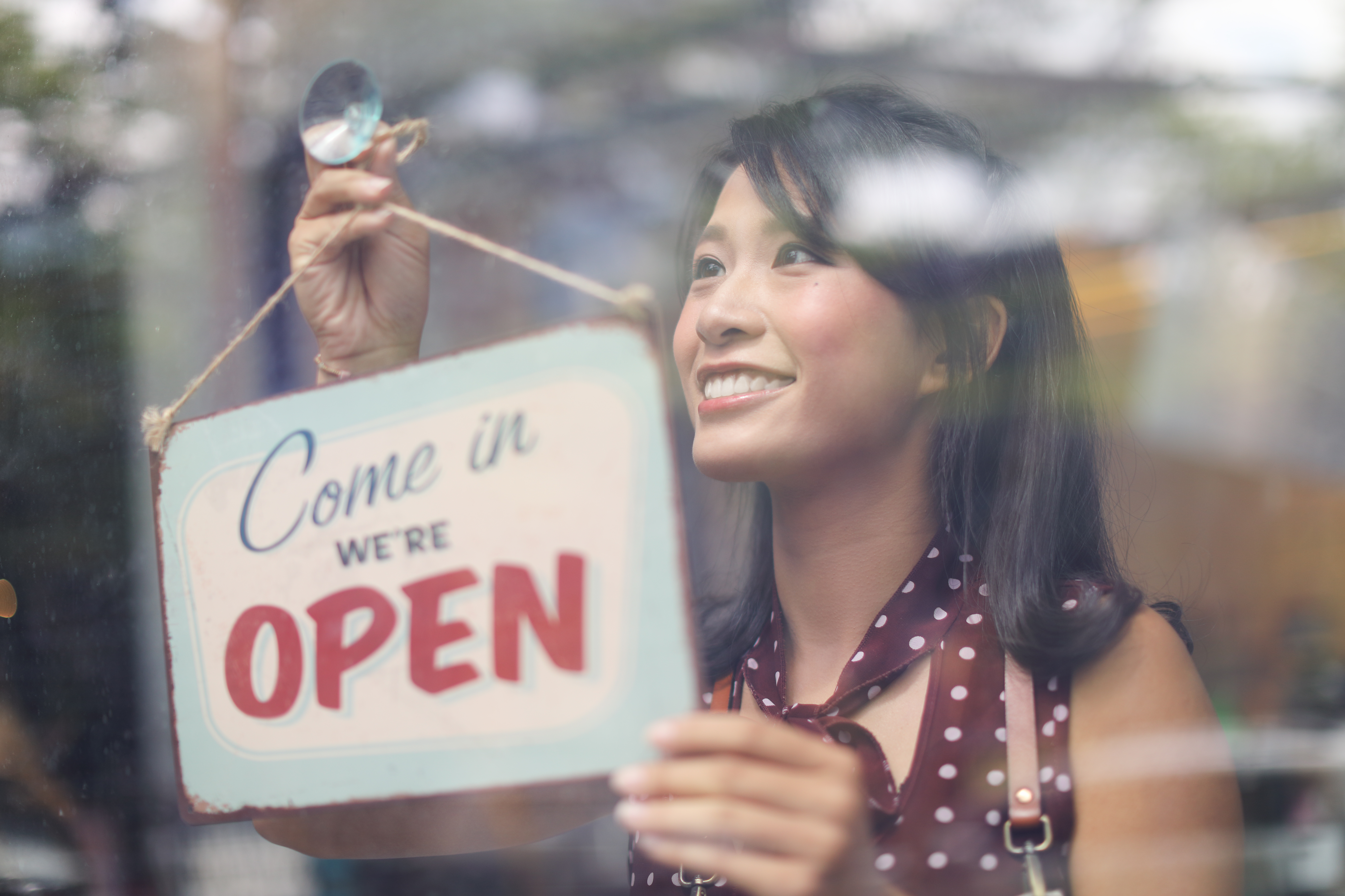 Woman hanging "Open" sign in door of small business
